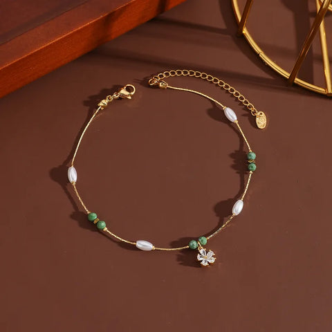 A dainty gold titanium anklet featuring a shimmering crystal flower charm accented by elegant white pearls and olive green beads.