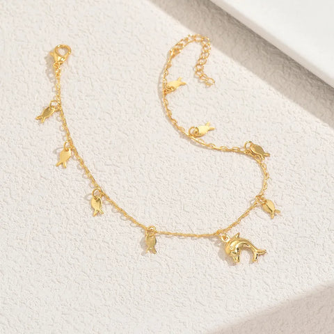 A playful gold-toned anklet featuring a central dolphin charm and multiple small fish dangles, perfect for adding a whimsical touch to your summer vacation wardrobe.