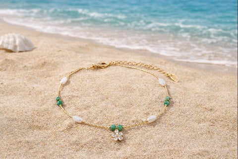 A delicate and feminine gold-toned anklet with a sparkling flower centerpiece and olive green accents, designed to add a graceful touch to your summer vacation.