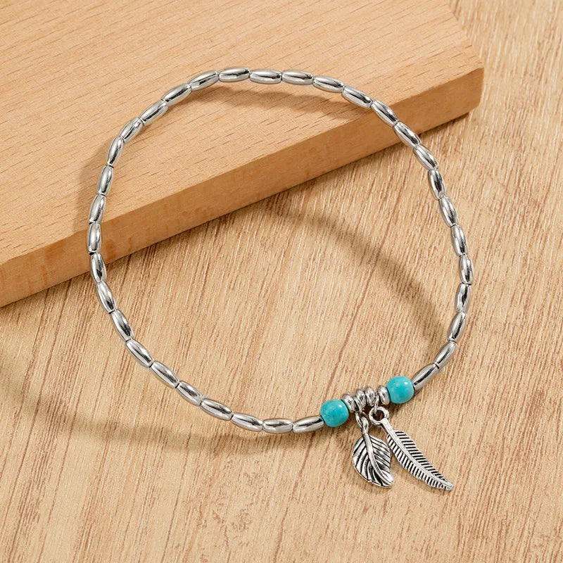 A vibrant turquoise seed bead anklet featuring a delicate gold-toned leaf charm.