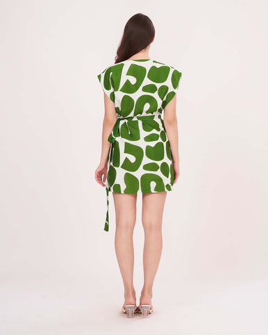 Rear view of a model wearing a short-sleeved mini dress featuring a bold green and white abstract pattern and a side-tie waist.